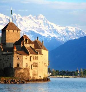a castle in the middle of a lake with a snow covered mountain