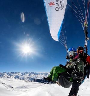 two people flying a parachute on top of a snow covered mountain