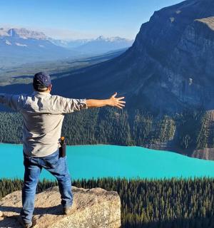 Ein Mann steht mit ausgestreckten Armen auf einem Berggipfel