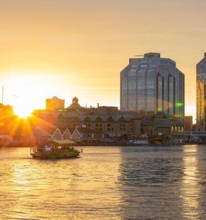 a city skyline with a boat in the water at sunset