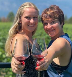 two women holding wine glasses in front of a vineyard