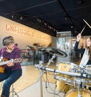 zwei Frauen spielen Schlagzeug und ein Mann spielt Gitarre