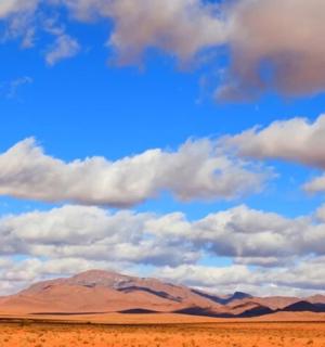 a view of a desert with a cloudy sky and mountains