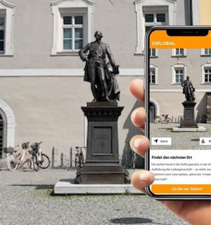 osoba držící mobilní telefon před sochou