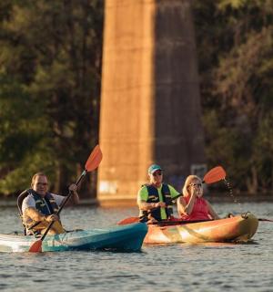 tři lidé v kajacích na vodě poblíž památníku