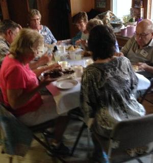 grupė žmonių, sėdinčių prie stalo ir valgančių