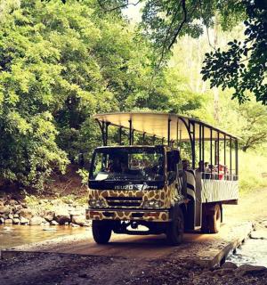 一辆卡车在土路上行驶，后面坐着人