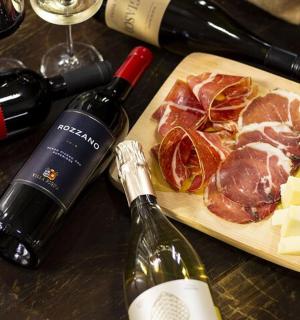 dřevěné prkénko s masem a sýrem a lahvemi vína