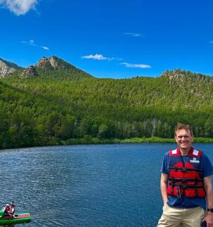 a man standing in front of a lake with a boat