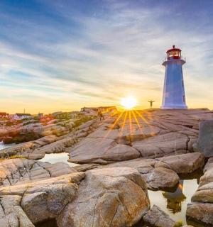 a lighthouse on a rocky shore with the setting sun