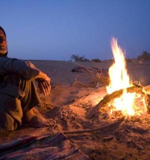 a man sitting next to a fire in the desert
