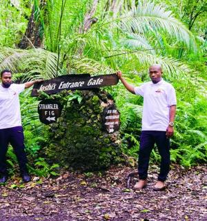 two men standing next to a sign in a forest