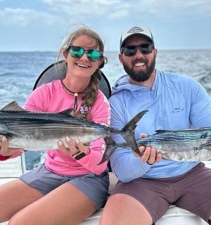 a man and woman sitting on a boat holding a fish