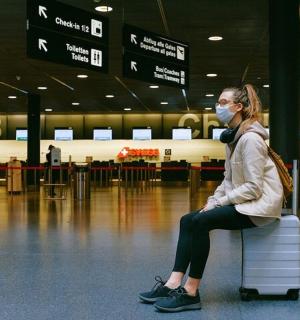 一名戴着口罩的女子坐在机场的行李箱上