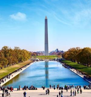 a group of people walking around a river with a monument in the background