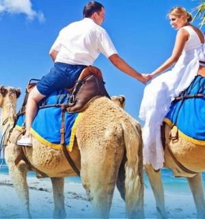 muž a žena jedoucí na velbloudech na pláži