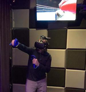 Човек стоји испред телевизора држећи микрофоне