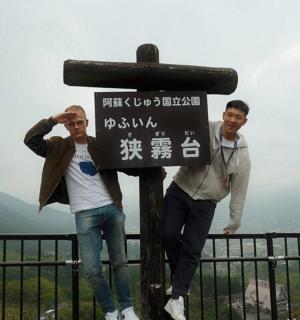 two men standing next to a sign on a mountain