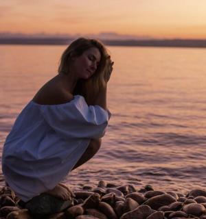 a woman in a white dress sitting on a rocky beach