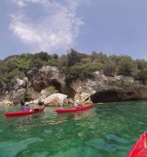 three people in red kayaks in the water near a cave