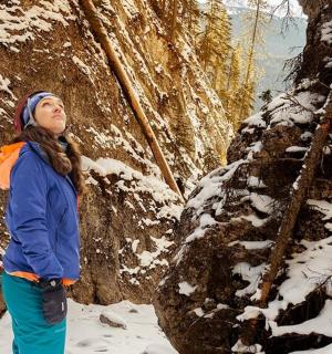 一名女子站在雪地里，旁边是一块岩石