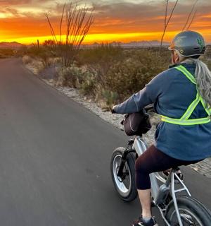 日落时分，一位女士骑着自行车沿着道路行驶