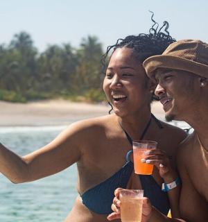 two women on the beach with drinks and a cell phone