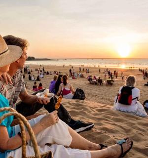 skupina lidí sedících na pláži a sledujících západ slunce