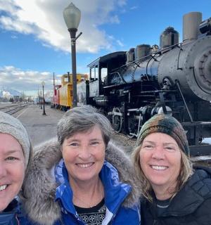 three women standing in front of an old train