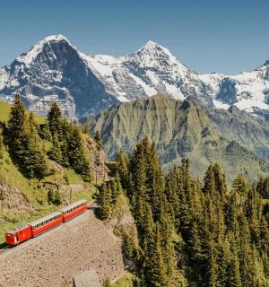 Červený vlak na kolejích s horami v pozadí