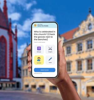 eine Person, die vor einem Gebäude ein Mobiltelefon hochhält
