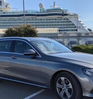 a silver car parked in a parking lot with a cruise ship