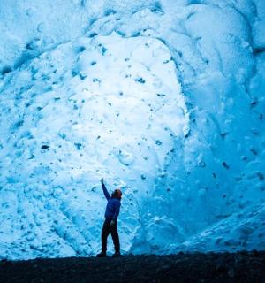 Un hombre está parado frente a una cueva de hielo.