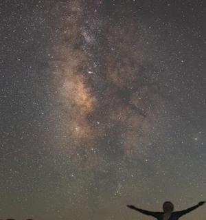 člověk stojící s rukama vztyčenýma před vesmírem