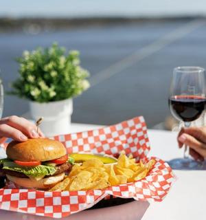 a person holding a hamburger and chips and a glass of wine