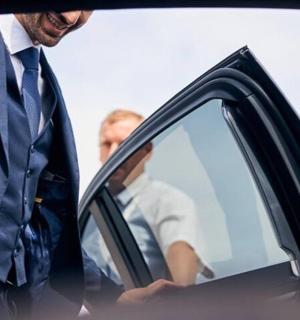 一名穿着西装的男子站在一辆汽车旁边