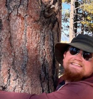 a man wearing a hat standing next to a tree