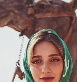 a woman wearing a green hijab standing in front of a camel