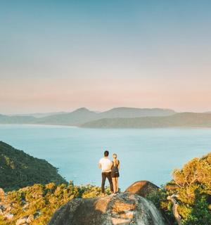 two people standing on a rock overlooking the ocean