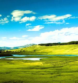 a green golf course with a river and mountains in the background