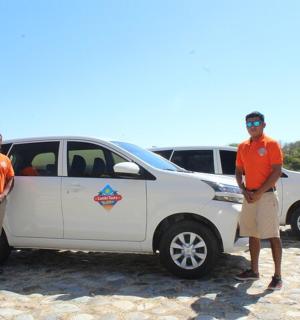 two men in orange shirts standing next to a white car