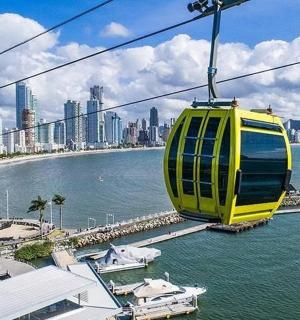a yellow cable car over the water with a city