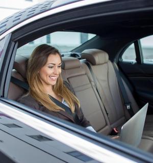 bir arabanın arka koltuğunda dizüstü bilgisayarla oturan bir kadın