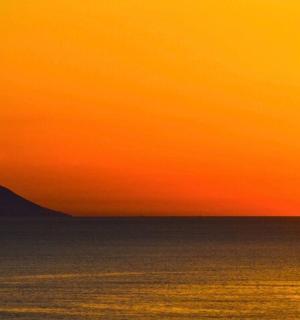 ein orangefarbener Sonnenuntergang über dem Meer mit einem Berg