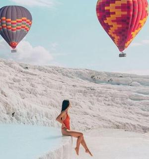 一名女子坐在海滩上，身边还有热气球