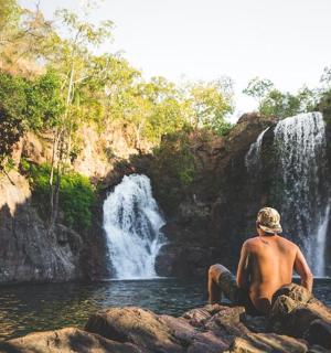 muž sedící na skalách před vodopádem