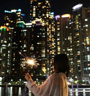 夜晚，一位女士在城市前手持烟花棒