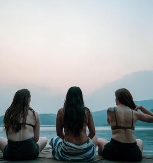 tři ženy sedící na molu s výhledem na vodní plochu