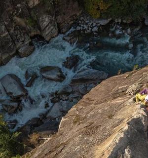 eine Person, die auf einem Felsen neben einem Fluss sitzt