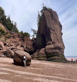 一个人站在海滩上,旁边是一块大石头